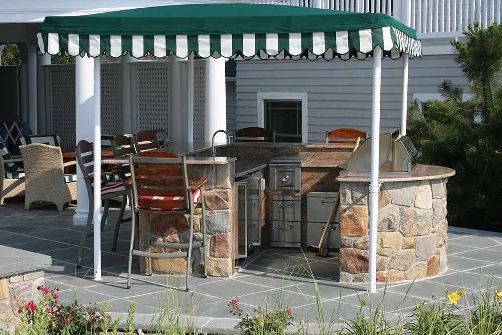 Outdoor patio with a green-striped canopy, stone bar, and chairs beside a house