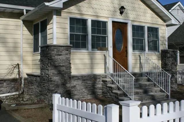 Front of a beige house with stone steps, white railings, and a white picket fence.