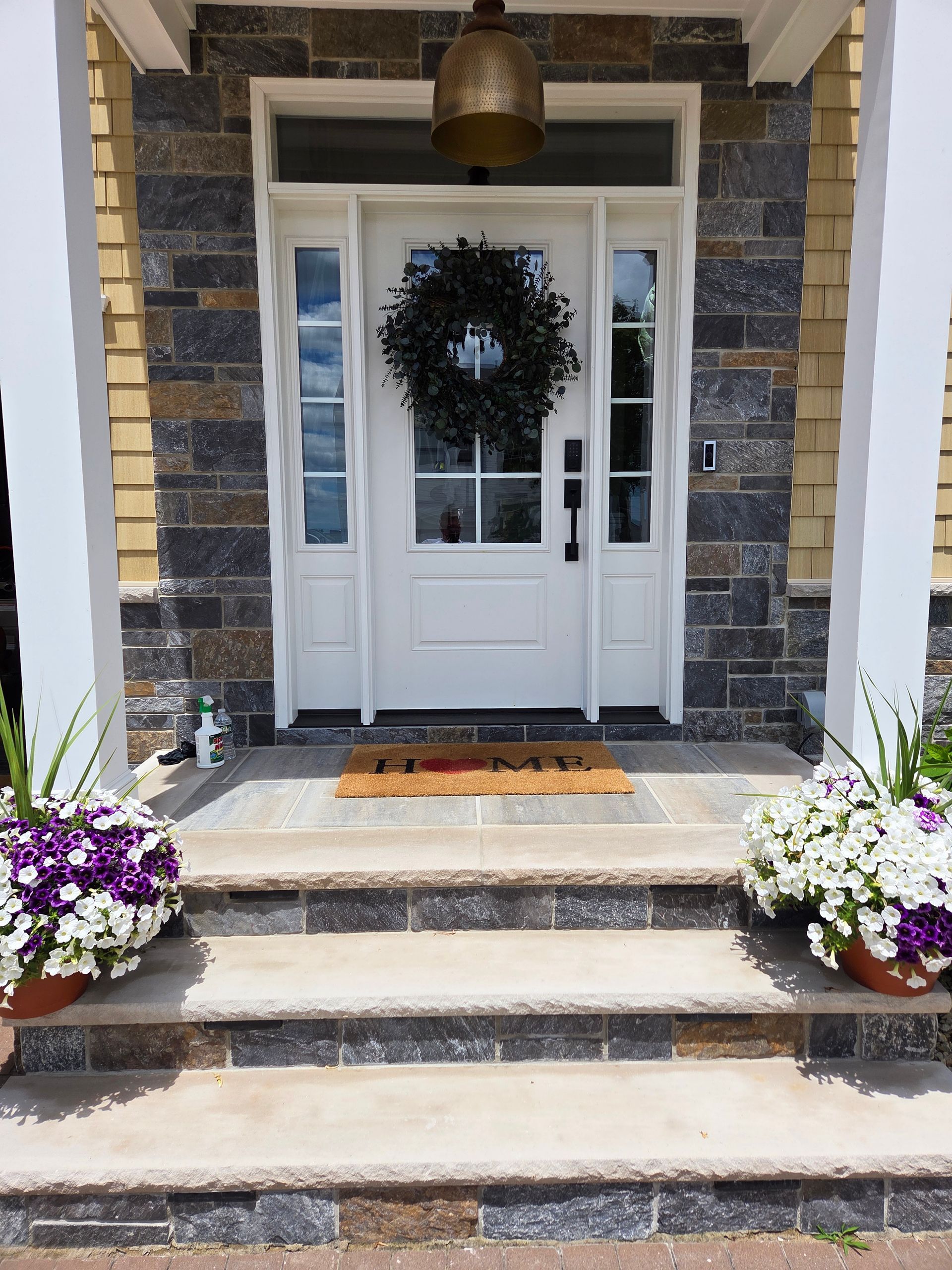 Front porch with white double doors, stone steps, hanging lantern, and purple and white flower pots.