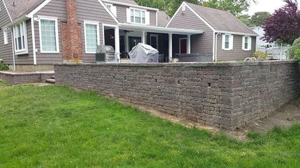 Stone retaining wall beside a suburban house with covered patio and green lawn