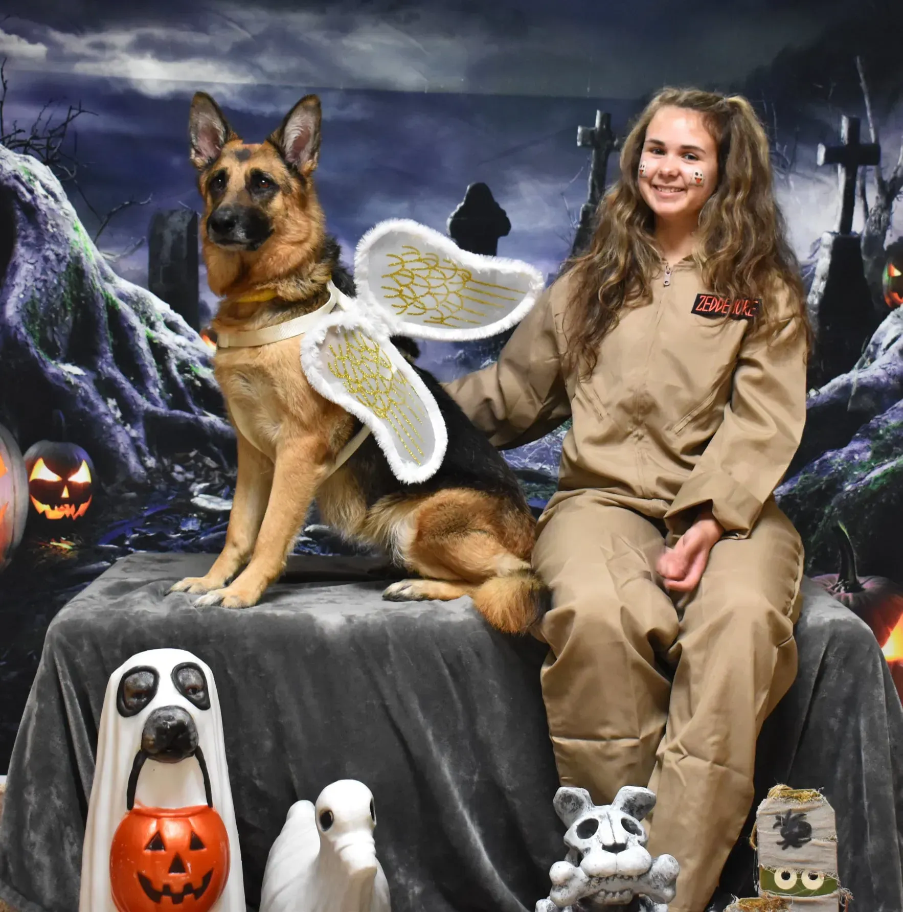 Girl with a German shepherd wearing angel wings, on a Halloween graveyard set with pumpkins and dog decorations