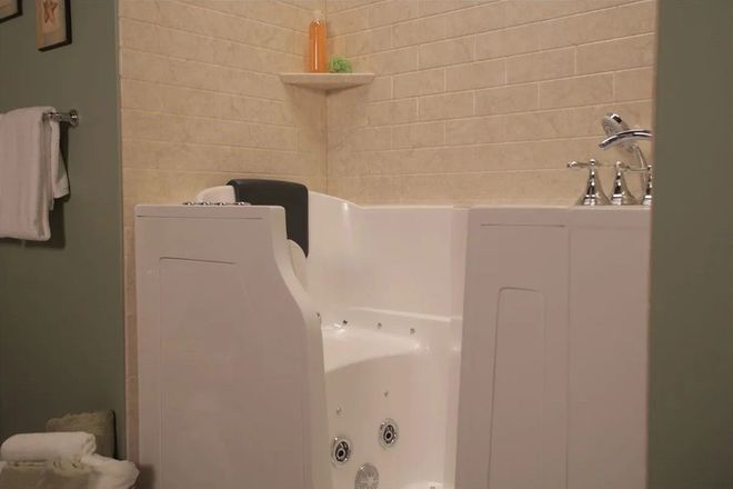 A white walk-in bathtub with a side door and built-in jets, installed in a bathroom with beige tiled walls.