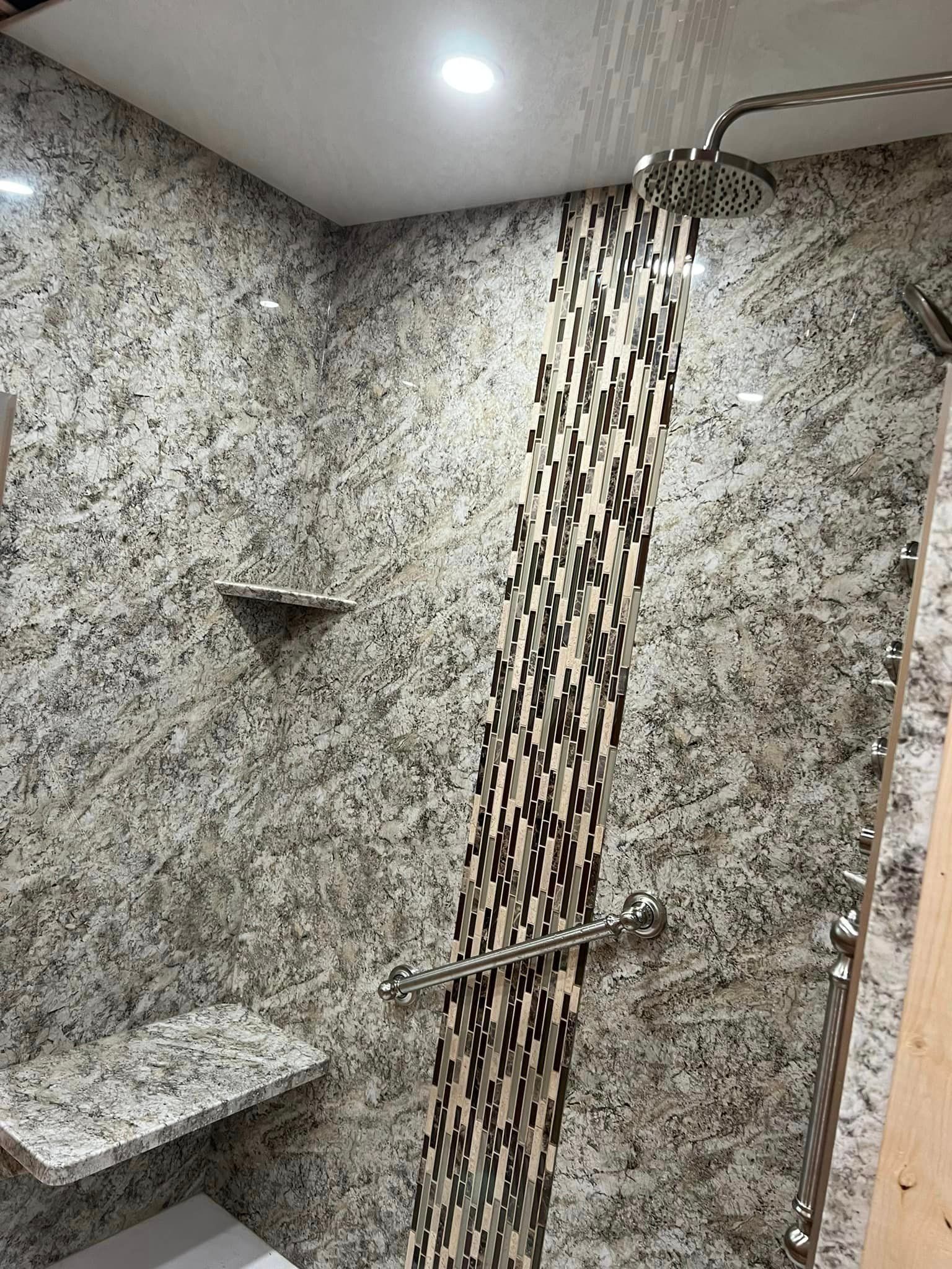 A walk-in shower with speckled granite walls, a central strip of patterned mosaic tile, a bench, and a rainfall showerhead.