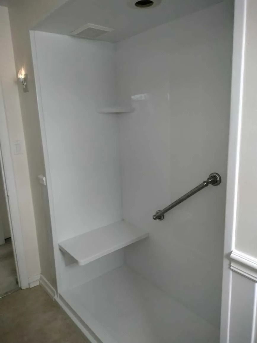 A white walk-in shower stall with an integrated bench and a diagonal metal grab bar on the side wall.