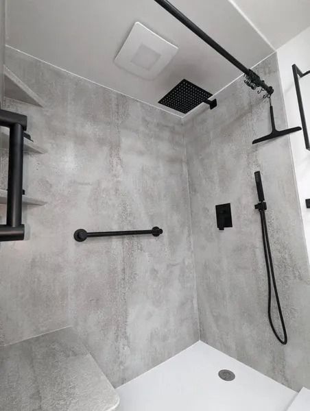A modern, accessible shower with grey stone-look walls, a white floor, a black grab bar, and black shower fixtures.