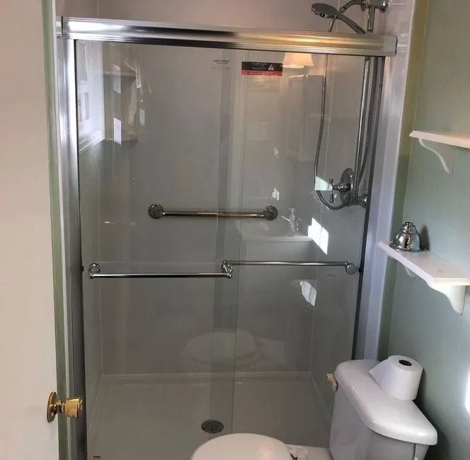 A glass shower enclosure with chrome hardware and a grab bar, positioned next to a white toilet in a light green bathroom.