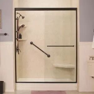 A walk-in shower with glass sliding doors, dark metal frame, wall-mounted grab bar, handheld showerhead, and built-in shelf.