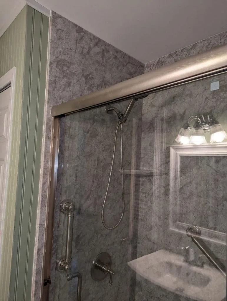 A bathroom featuring a glass shower door with metallic trim, a handheld showerhead inside, and a sink reflected in the glass.