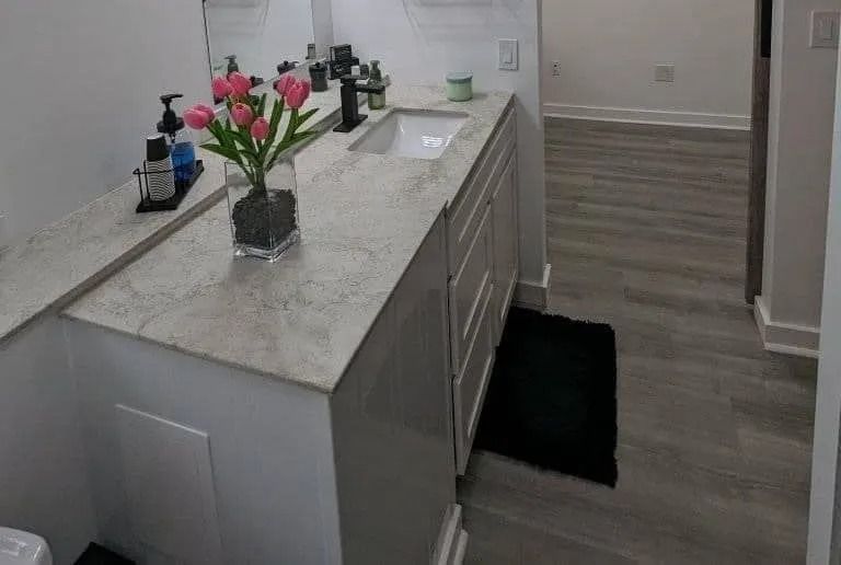 A modern bathroom with a light stone countertop, a white vanity cabinet, a sink, and a vase of pink tulips.