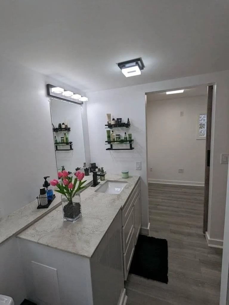 A modern bathroom vanity with a speckled countertop, flowers in a vase, wall shelves, and an open doorway.