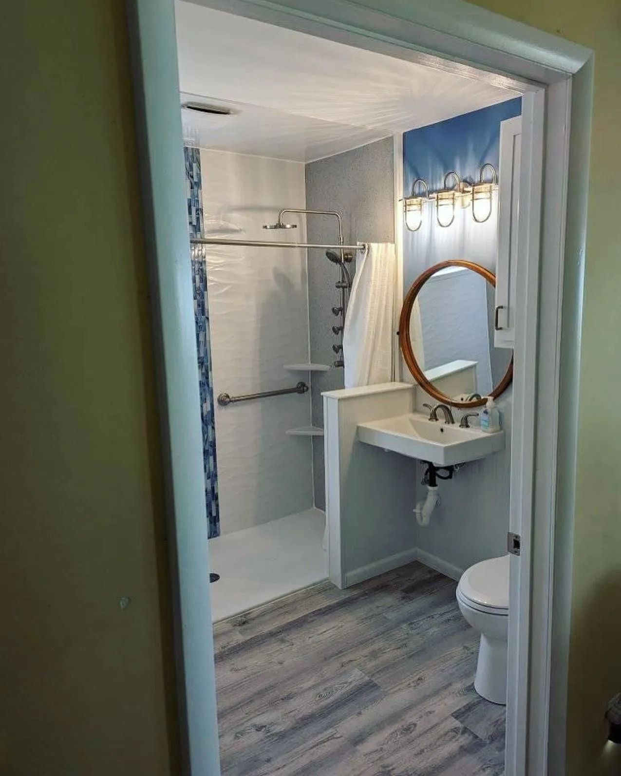 A bathroom viewed through a doorway, featuring a walk-in shower with grab bars, a floating sink, and a white toilet.