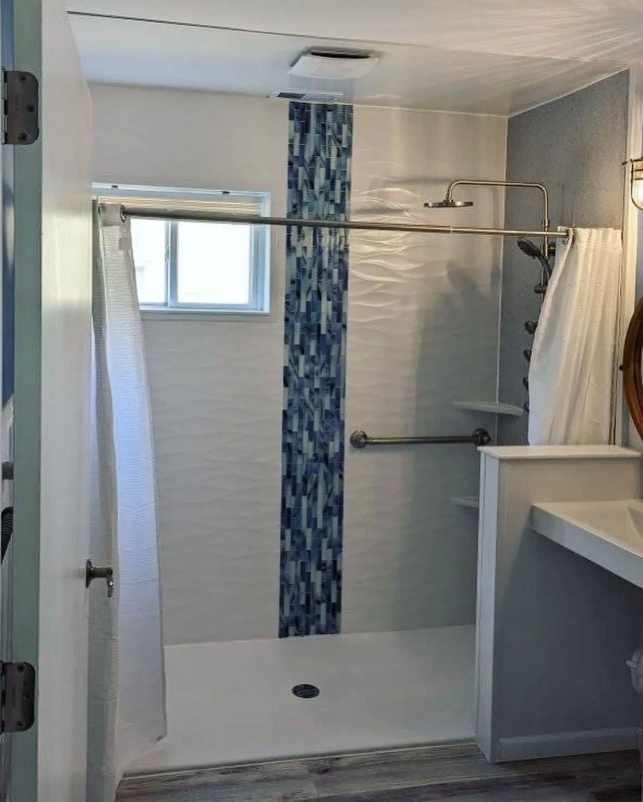 A walk-in shower with a white floor, blue vertical mosaic accent tile, white walls, a grab bar, and a window.