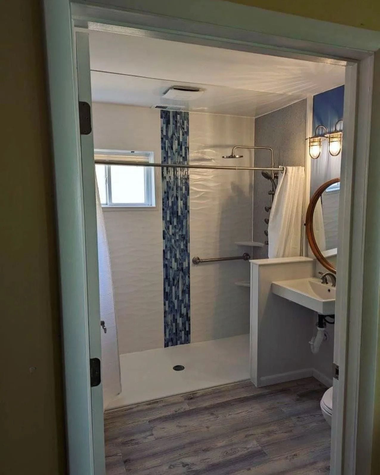 A bathroom featuring a walk-in shower with a blue tile accent, a wall-mounted sink, and gray wood-look flooring.