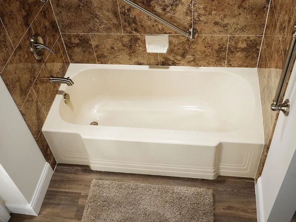 A beige bathtub installed between tiled walls, featuring a faucet, drain, and grab bars in a bathroom with wood flooring.