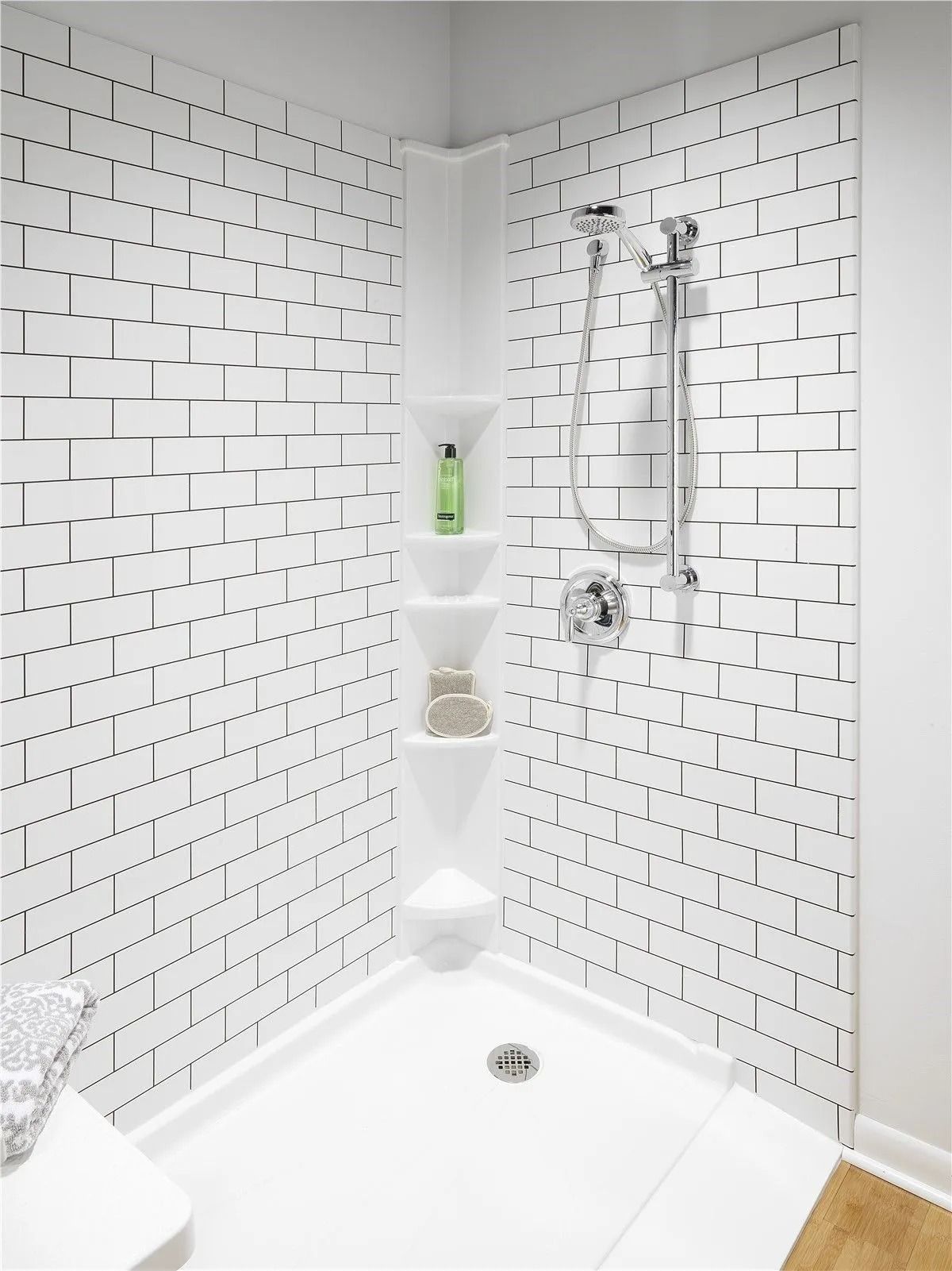A corner shower unit with white, subway tile-patterned walls, a built-in five-shelf organizer, and a silver shower head.