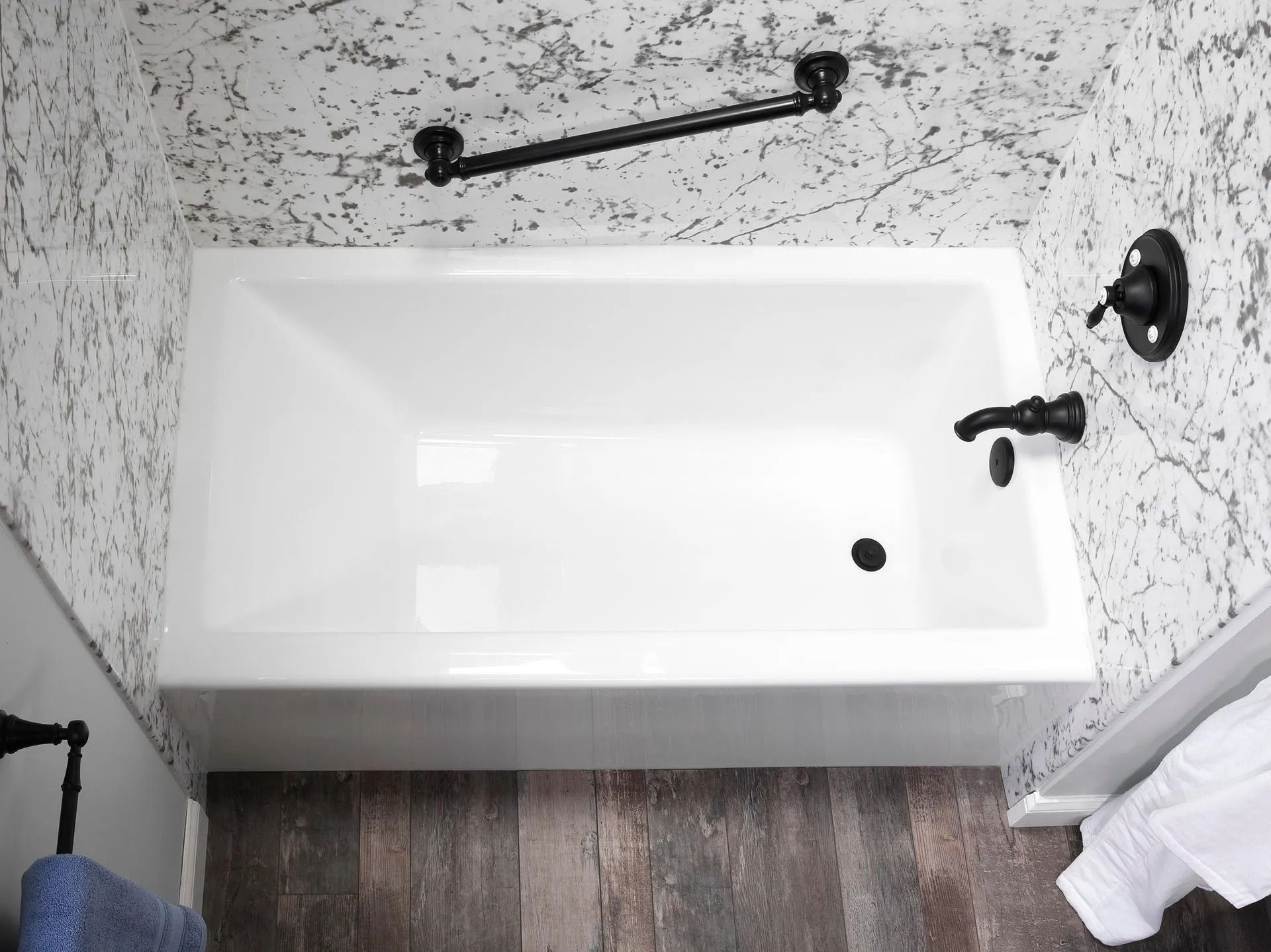 A white bathtub against a marble-patterned wall, featuring a black faucet, handles, and a horizontal grab bar.