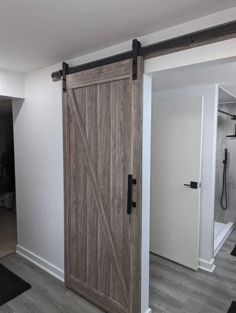 A sliding wooden barn door with a black metal track and handle installed in a modern home hallway.