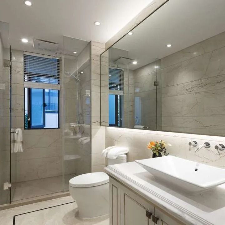 A bright, modern bathroom featuring a vessel sink, large vanity mirror, toilet, and a glass-enclosed shower.