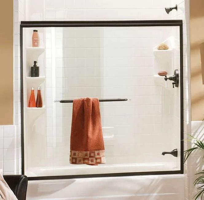 A sliding glass bathtub door with a dark frame and handle, featuring a hanging brown towel in a white bathroom setting.