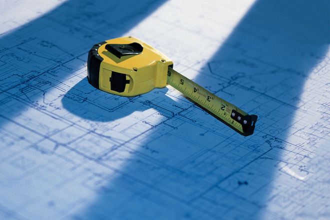 A yellow tape measure sitting on top of architectural blueprints, cast in partial shadows.