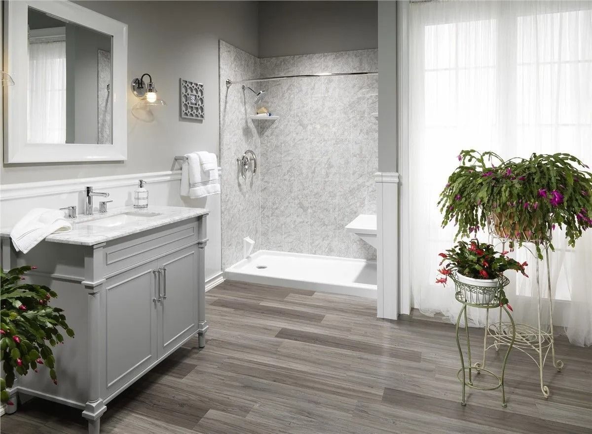 Modern bathroom with gray vanity, marble-patterned walk-in shower, wood-look flooring, and a potted plant on a metal stand.