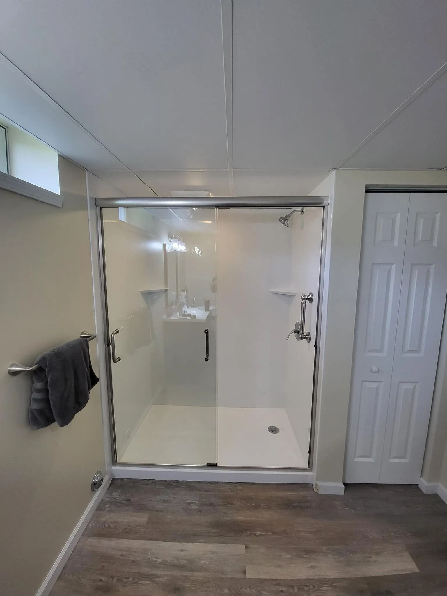 A modern bathroom featuring a white walk-in shower with a glass door, light-colored walls, and wood-look flooring.