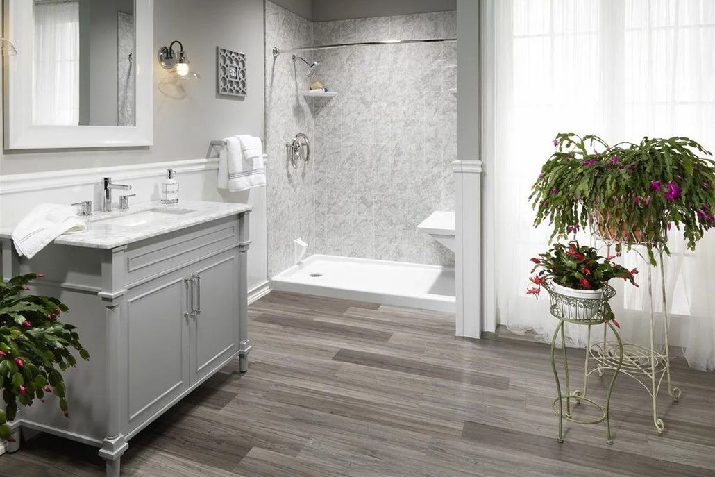 A modern gray bathroom with a marble vanity, a glass-enclosed shower with tiled walls, and a potted plant on a stand.