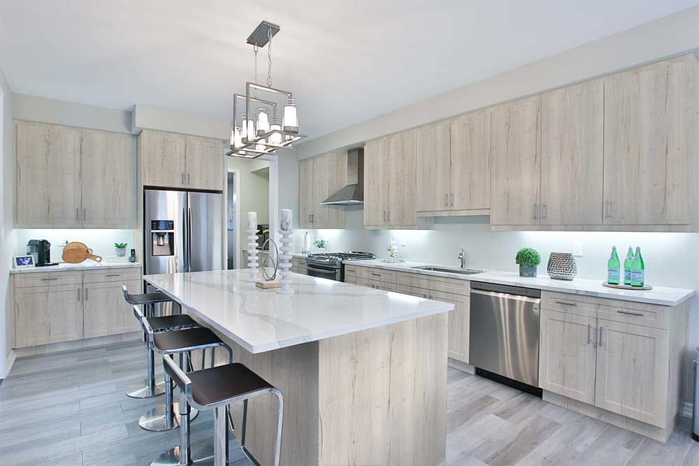 Modern kitchen with light wood cabinets, white countertops, stainless steel appliances, and a central island with stools.