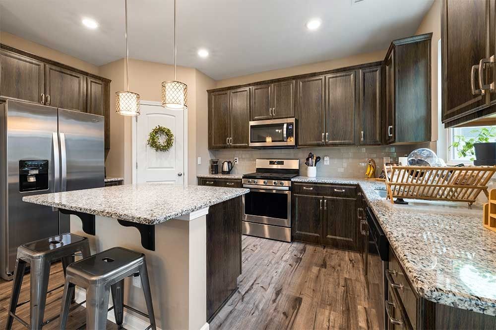 Modern kitchen with dark wood cabinets, granite countertops, stainless steel appliances, and a breakfast bar with stools.