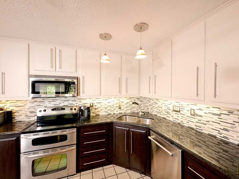 A modern kitchen featuring dark lower cabinets, white upper cabinets, stainless steel appliances, and a tiled backsplash.