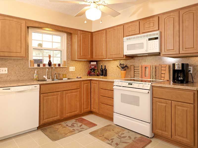 A kitchen featuring honey-oak cabinets, white appliances, a tiled backsplash, and a window above the sink.