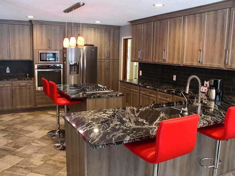 Modern kitchen with wood cabinets, dark marble countertops, three red bar stools, and stainless steel appliances.