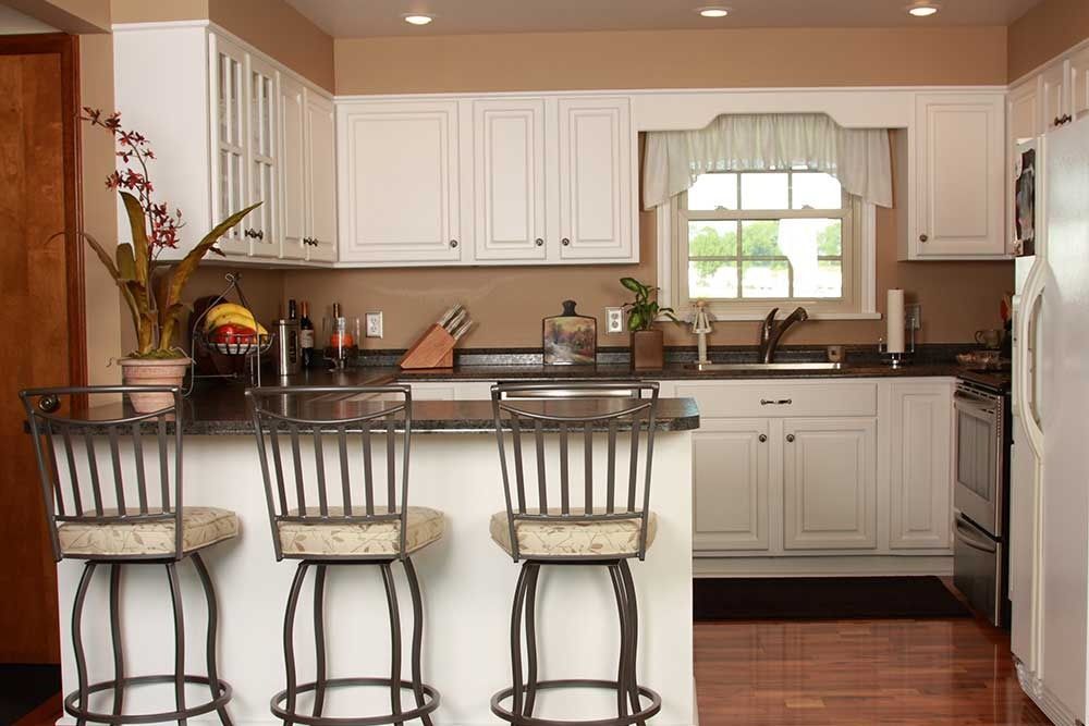 A kitchen with white cabinets, dark countertops, hardwood floors, and a breakfast bar with three stools.