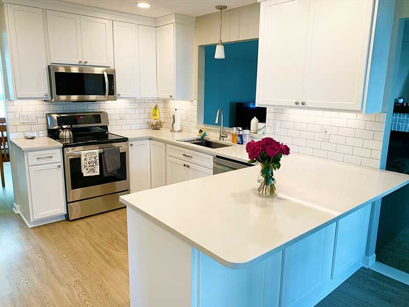 A modern kitchen with white cabinets, light countertops, a stainless steel range, and a vase of flowers on an island.