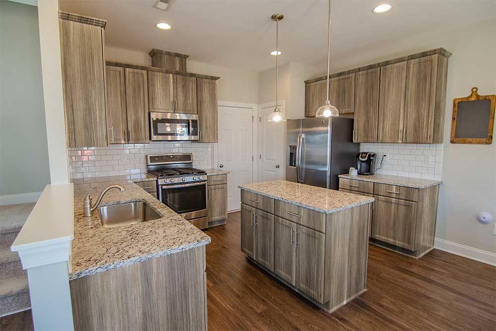 A modern kitchen featuring light wood cabinetry, speckled granite countertops, stainless steel appliances, and an island.