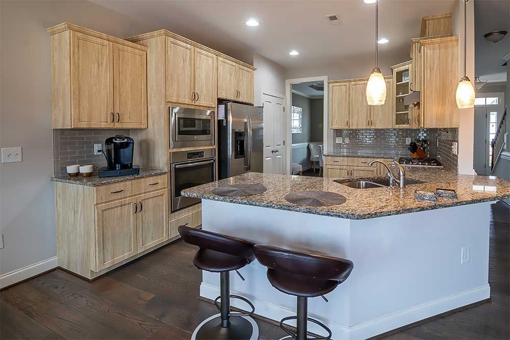 A modern kitchen with light wood cabinets, granite countertops, stainless steel appliances, and two brown bar stools.