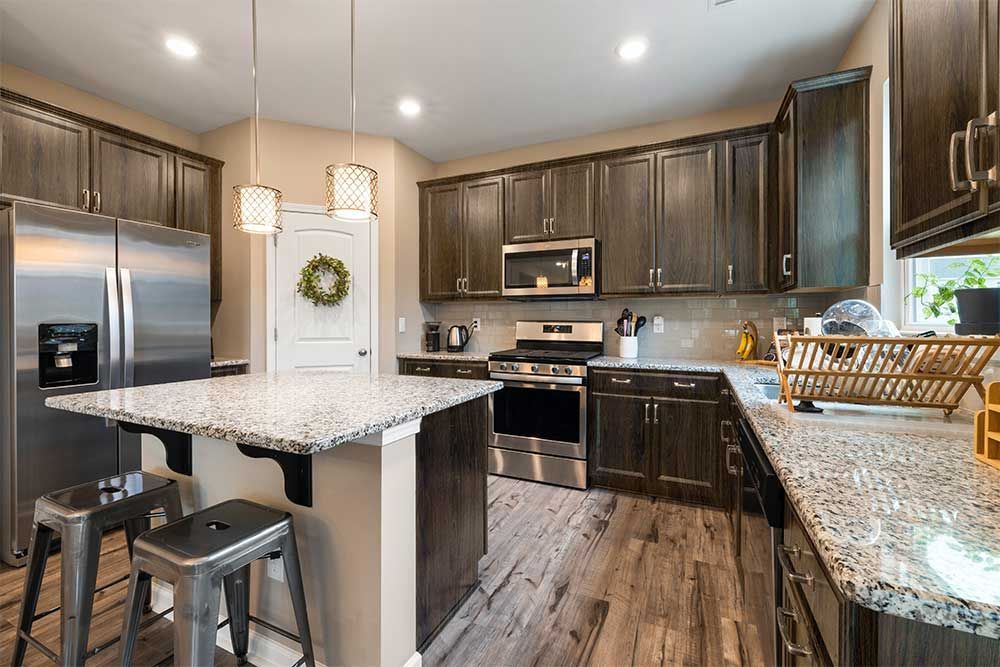 Modern kitchen featuring dark wood cabinets, granite countertops, a central island with metal stools, and steel appliances.