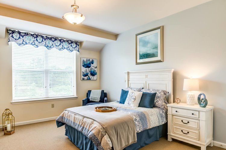 A bedroom with a bed , nightstand , chair and window.