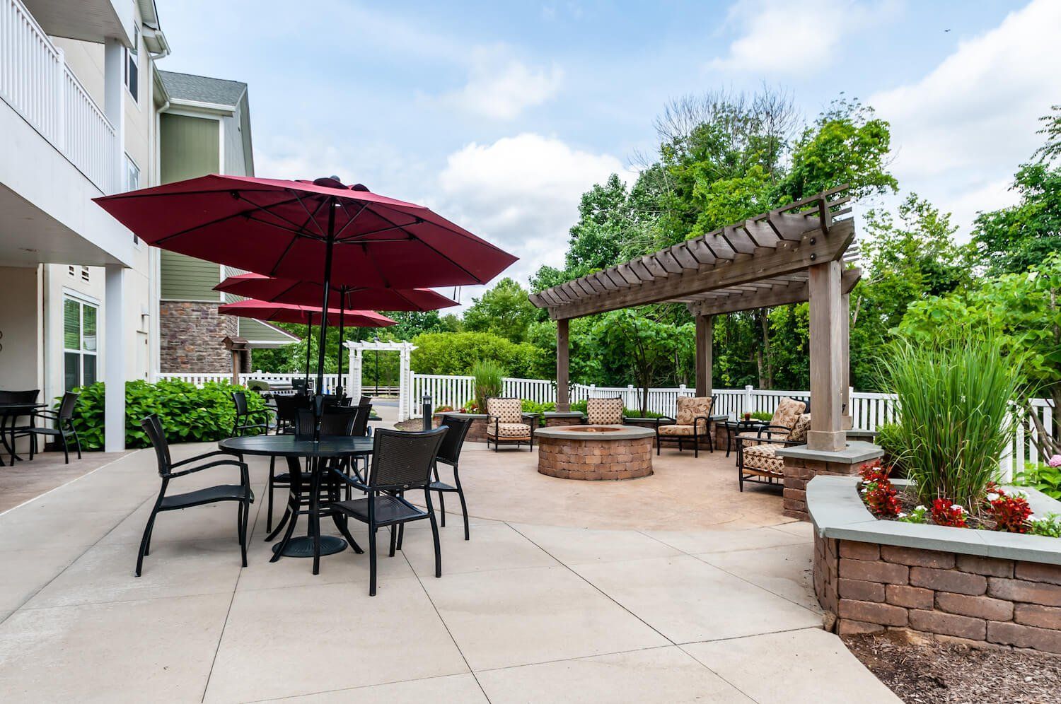 A patio with tables , chairs , umbrellas and a fire pit.