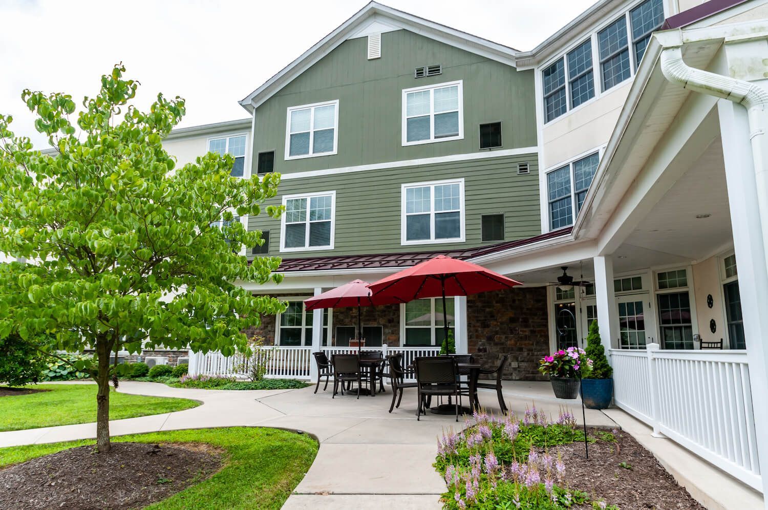 A large green building with a porch and tables and chairs under red umbrellas.