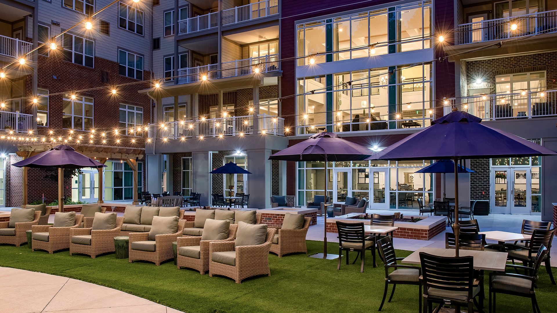 A large building with tables and chairs and umbrellas in front of it.