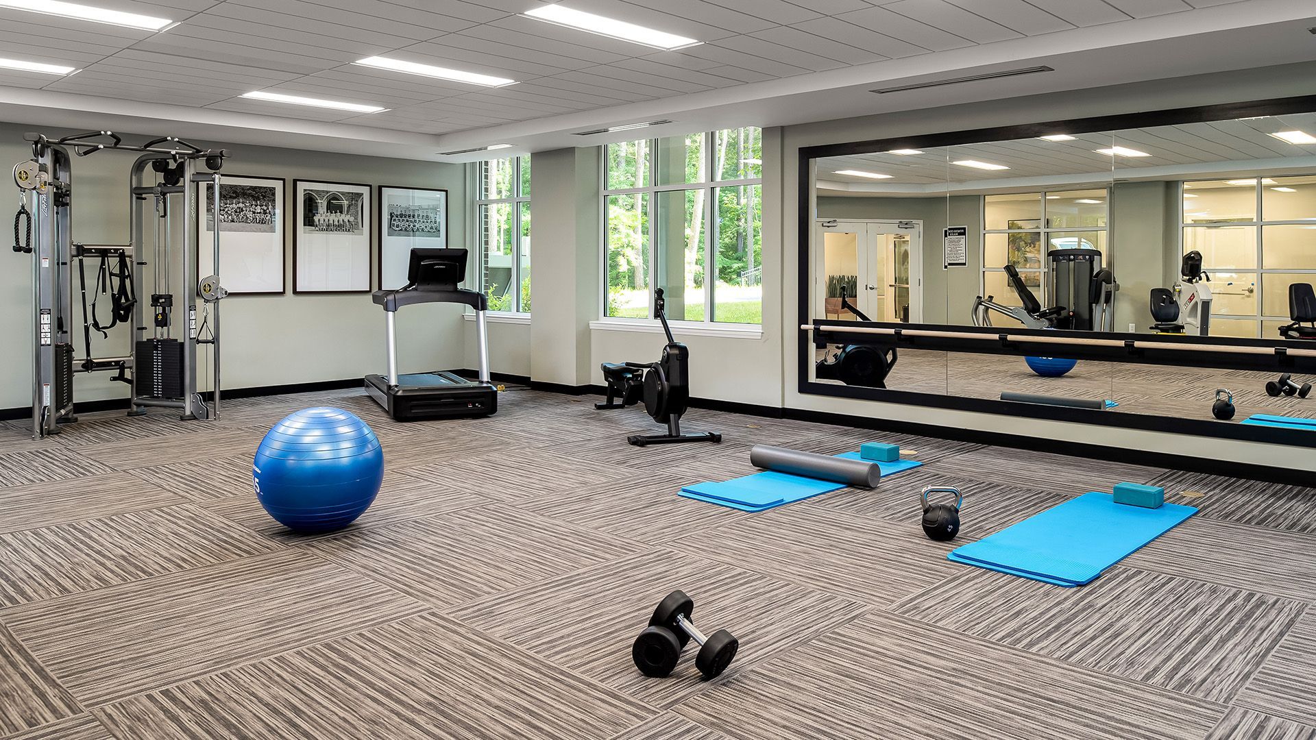 A gym with a treadmill , a pilates ball , a yoga mat , and a large mirror.