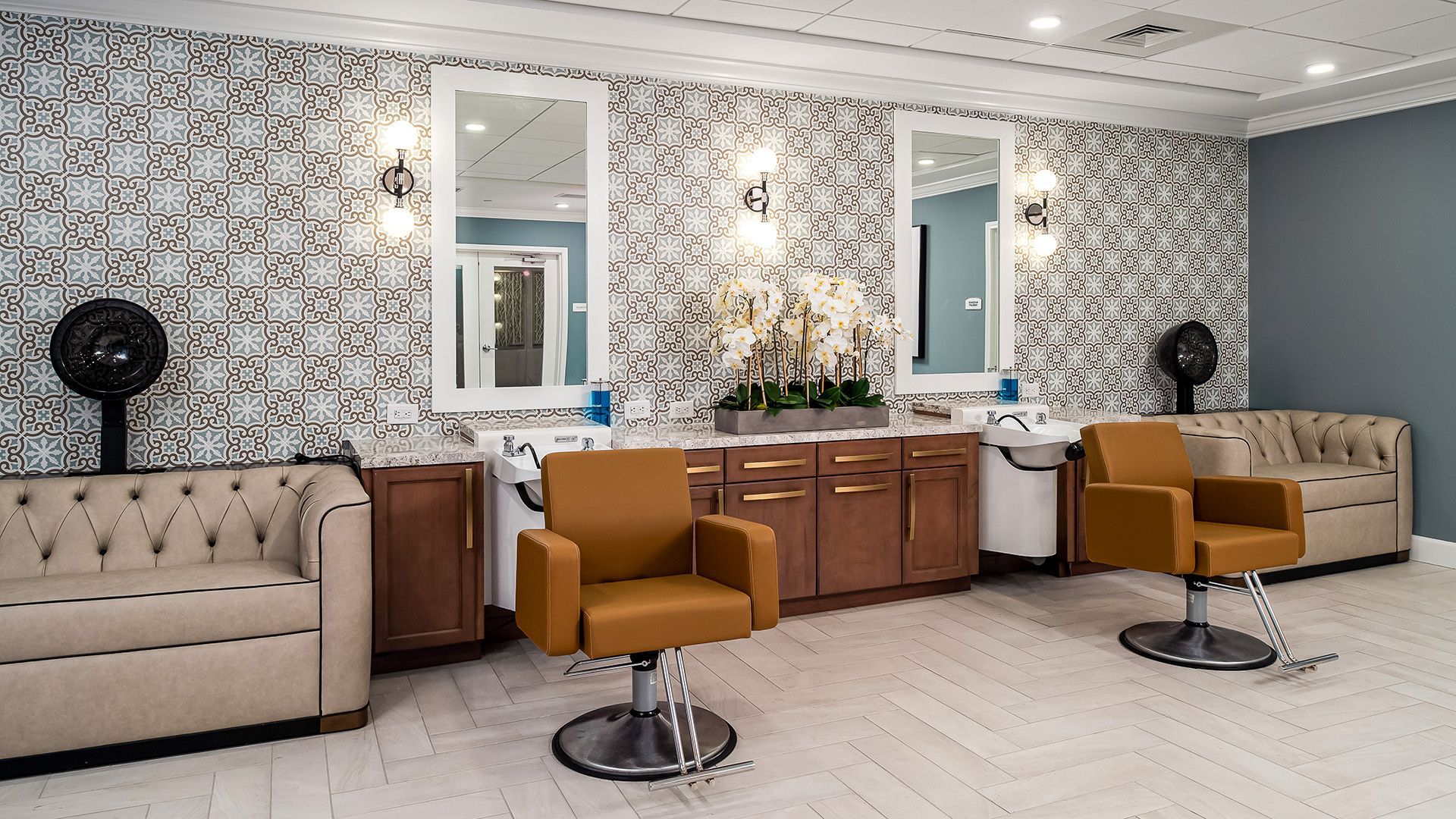 A salon with two chairs , a couch , and mirrors.