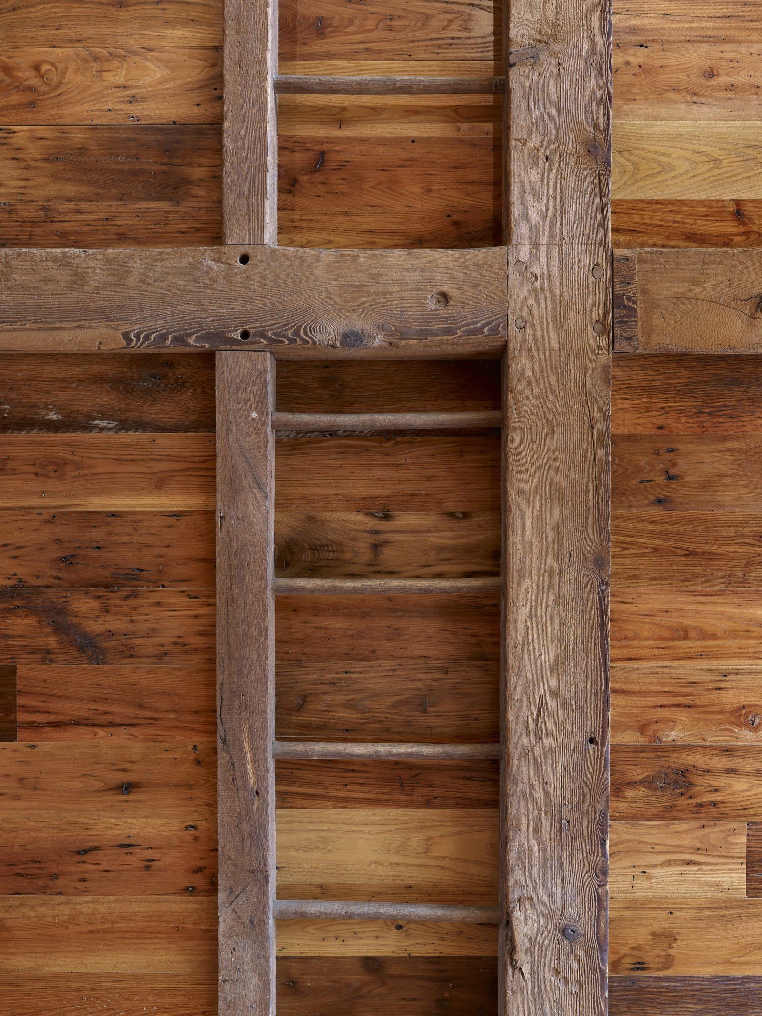 A wooden ladder is hanging on a wooden wall.