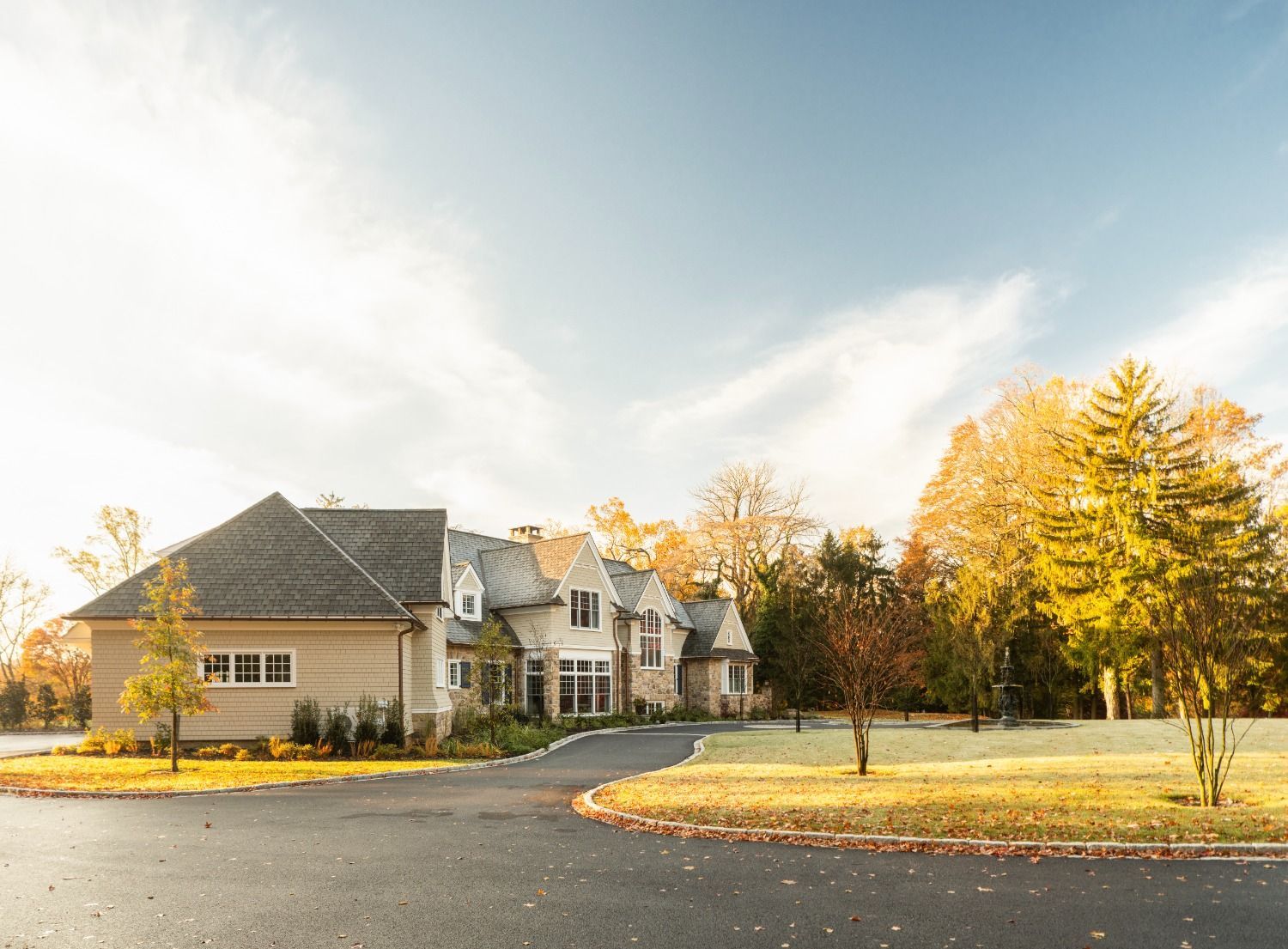 A large house is sitting on top of a lush green field surrounded by trees.