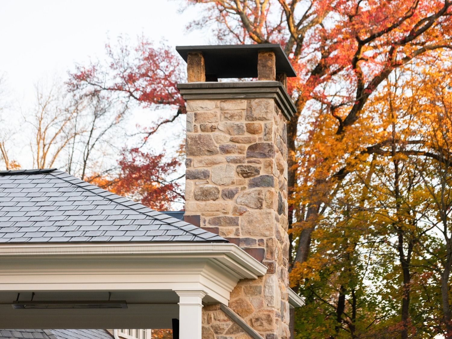 A stone chimney on the side of a house with trees in the background