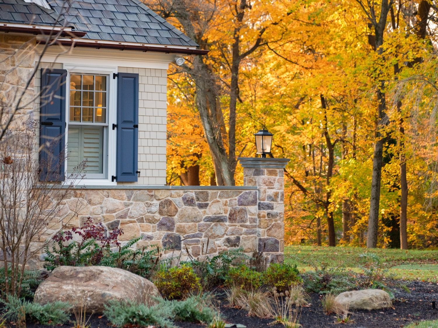 A house with blue shutters is surrounded by trees with yellow leaves.