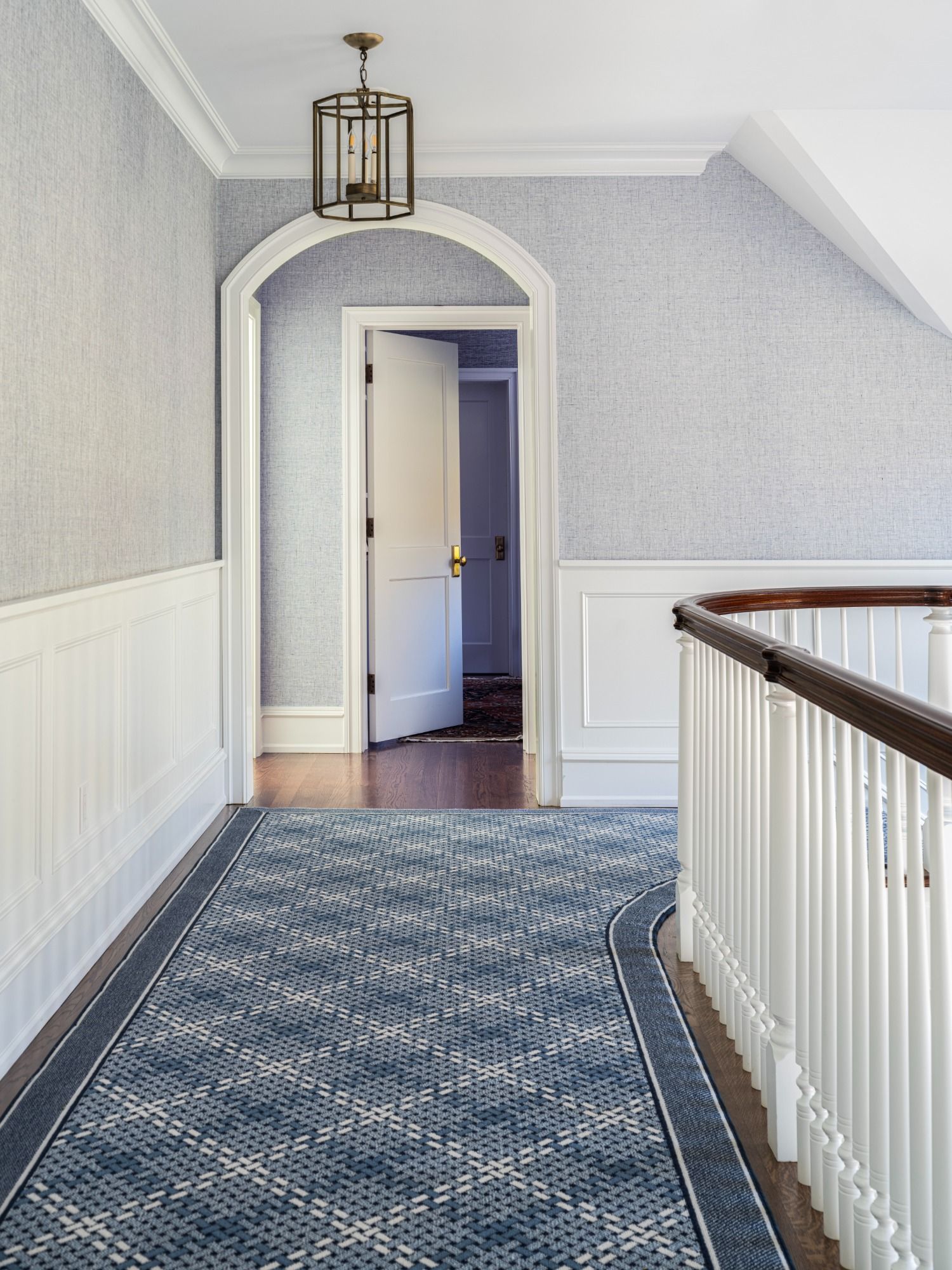 A hallway with a blue rug and a white railing