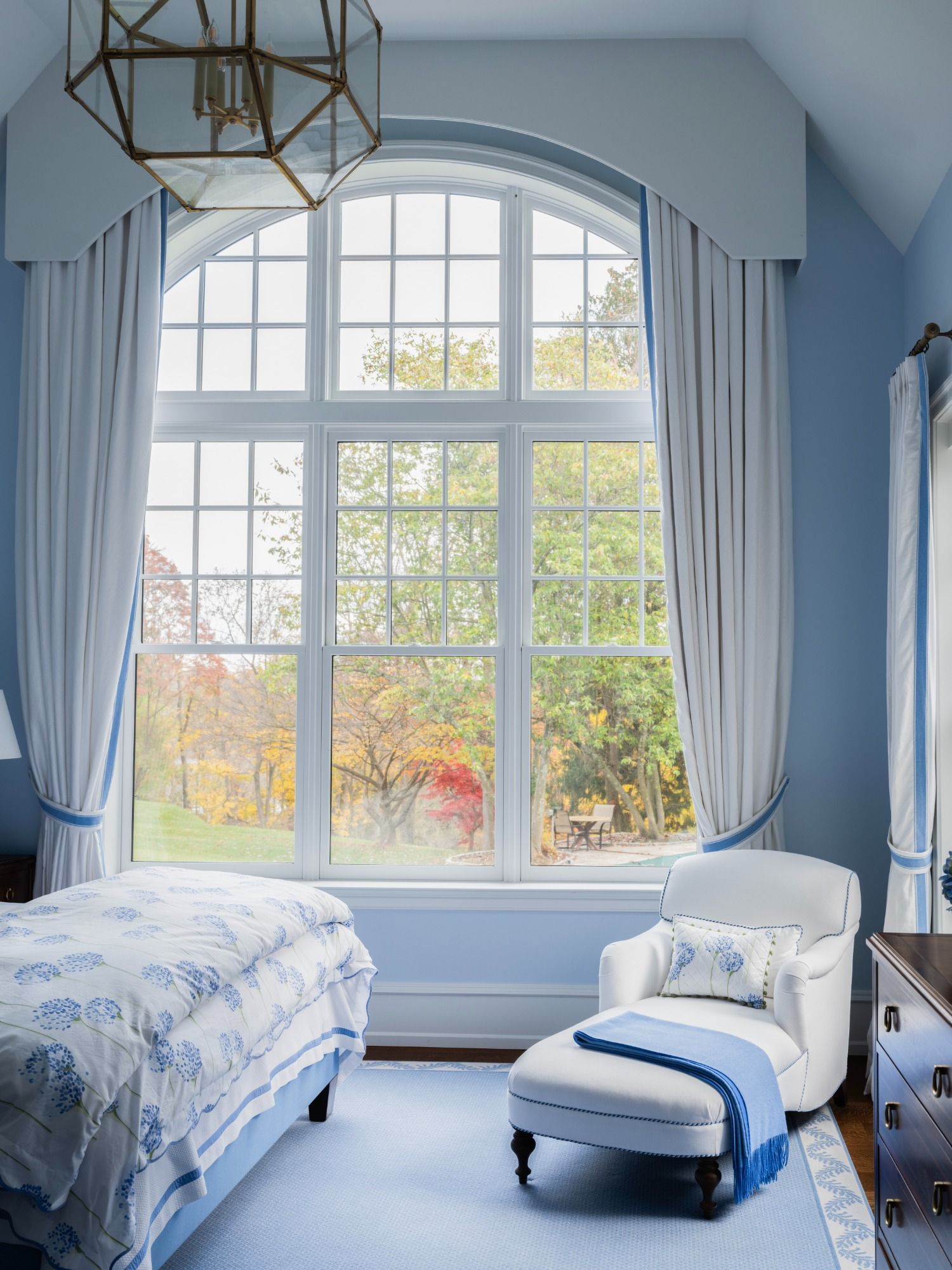 A bedroom with a bed , chair , ottoman and large window.