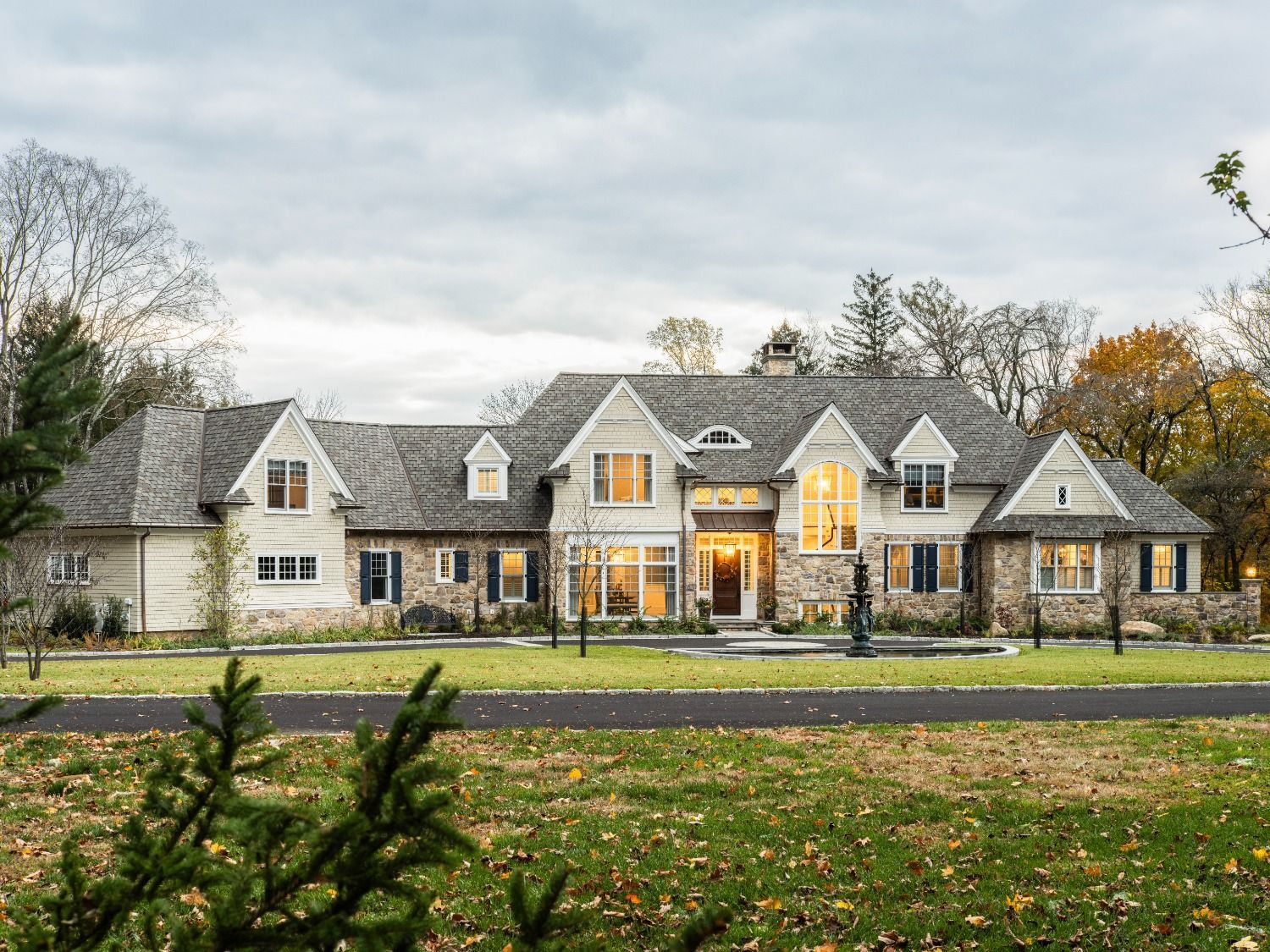 A large white house with a gray roof is sitting on top of a lush green field.